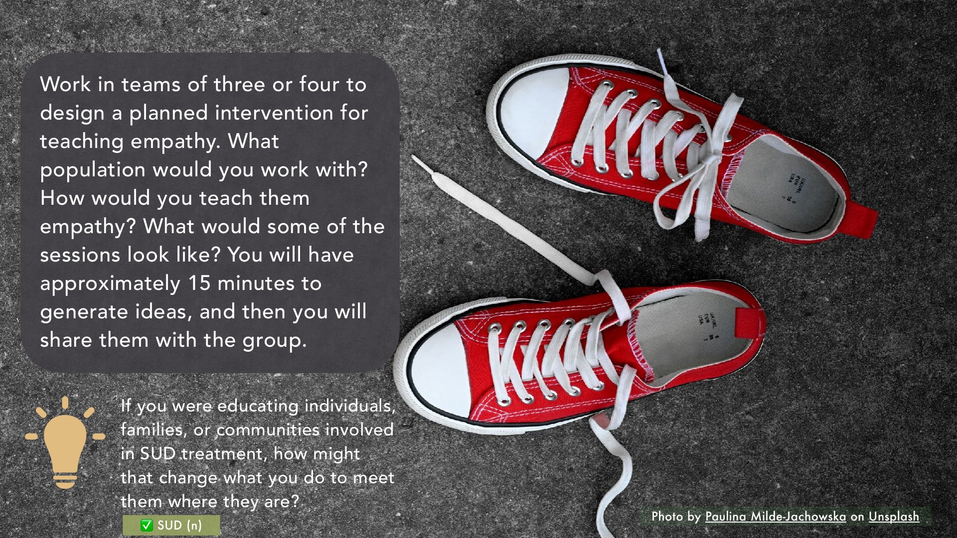 A presentation slide displays team instructions for designing an empathy-teaching intervention in white text boxes, with prompts about target populations and SUD treatment education, alongside a photograph of red and white canvas high-top sneakers on a gray textured background.