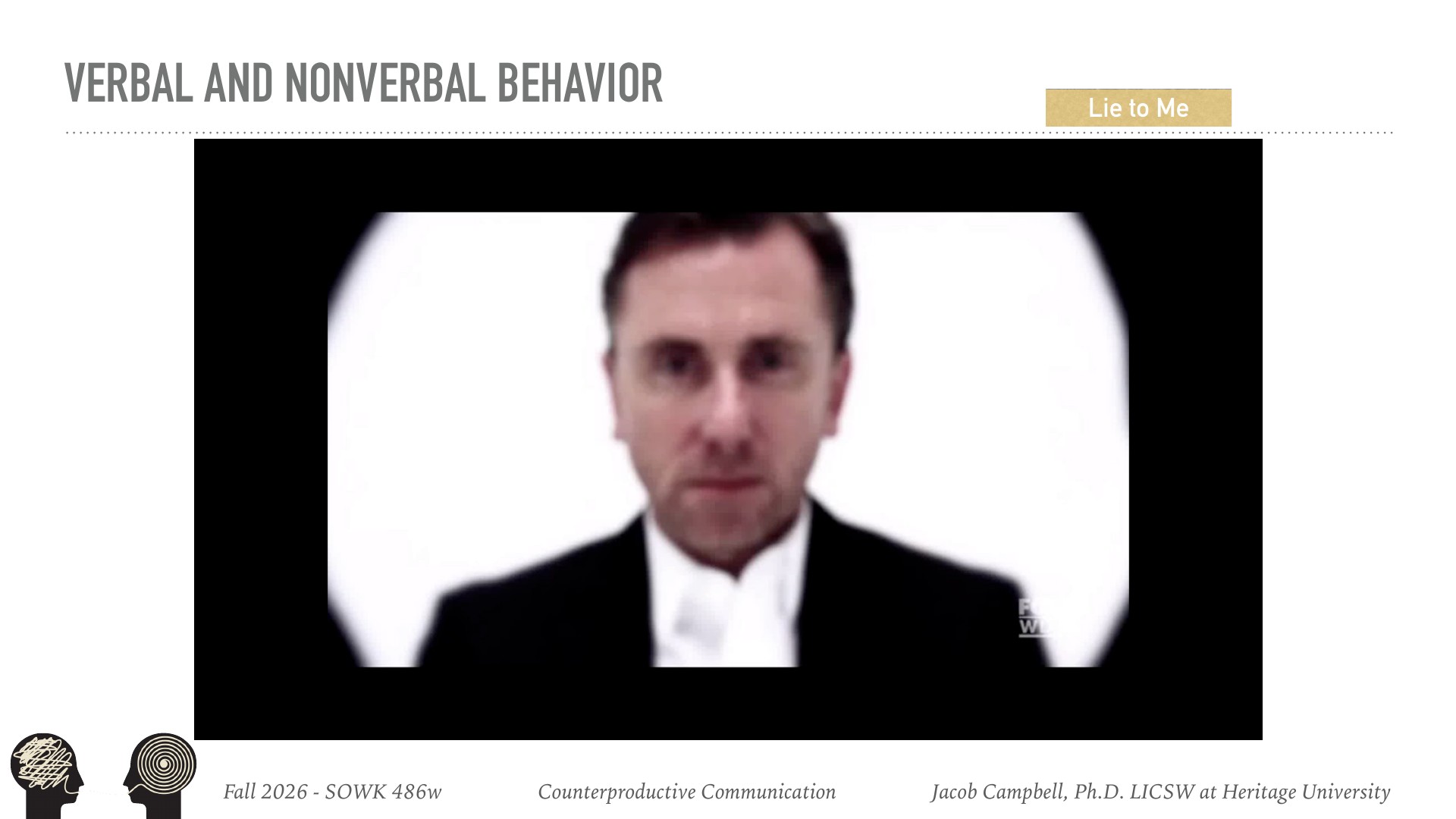 A man in formal black suit and white shirt displays a serious facial expression while looking directly at the camera against a white background. The slide is titled 'VERBAL AND NONVERBAL BEHAVIOR' with 'Lie to Me' referenced in the upper right, from Fall 2026 SOWK 486w on Counterproductive Communication taught by Jacob Campbell, Ph.D. LICSW at Heritage University.