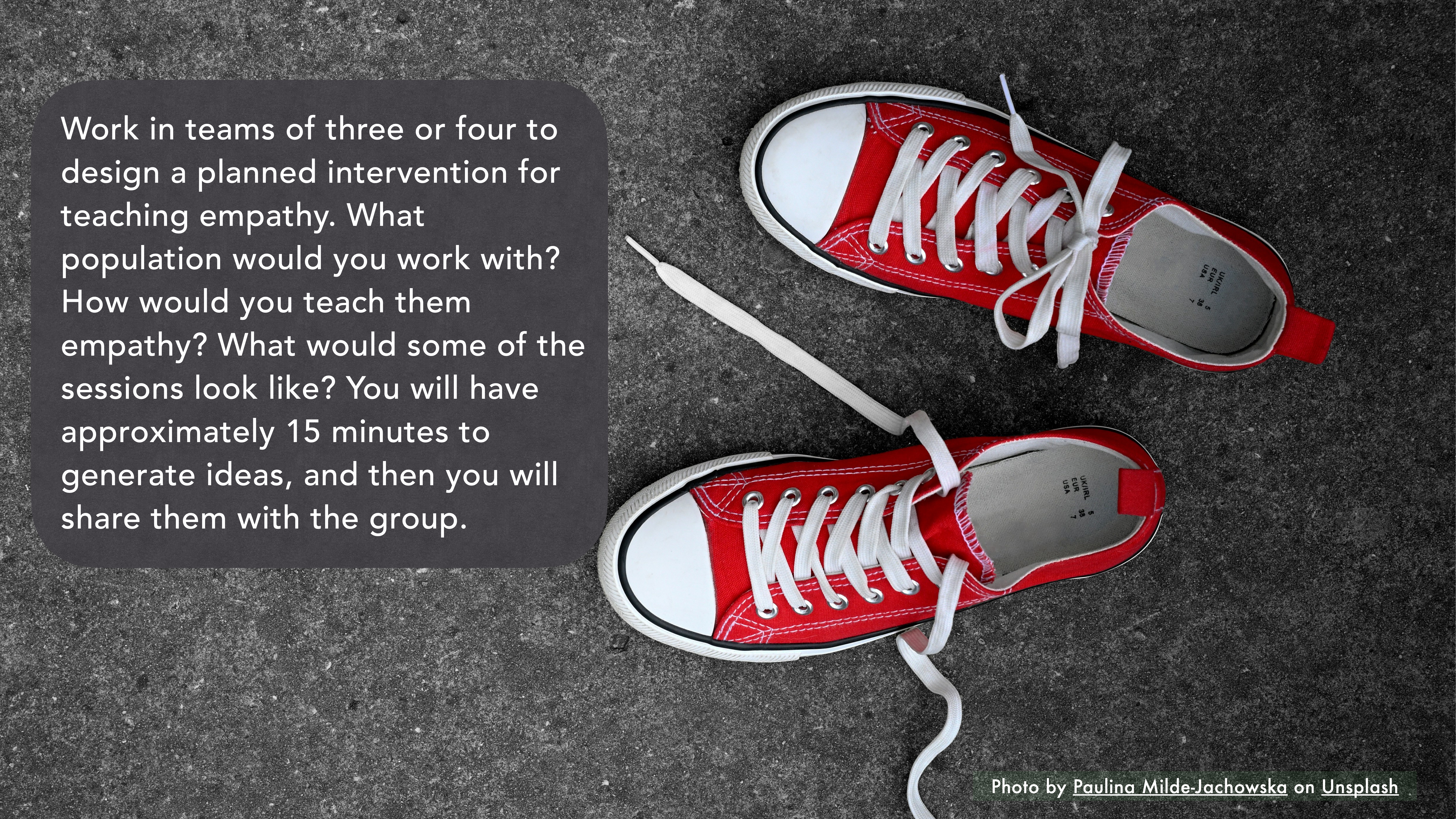 Red sneakers rest on a gray concrete surface. Text beside them reads: 'Work in teams of three or four to design a planned intervention for teaching empathy. What population would you work with? How would you teach them empathy? What would some of the sessions look like? You will have approximately 15 minutes to generate ideas, and then you will share them with the group.' Photo credit: Paulina Milde-Jachowska on Unsplash.